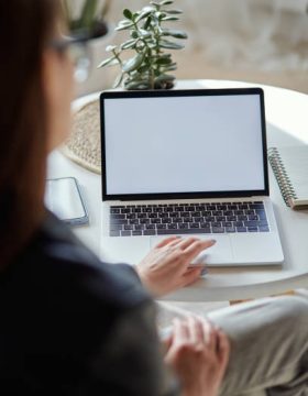 Mockup white screen laptop and mobile phone woman using computer sitting at table at home, back view, focus on screen.